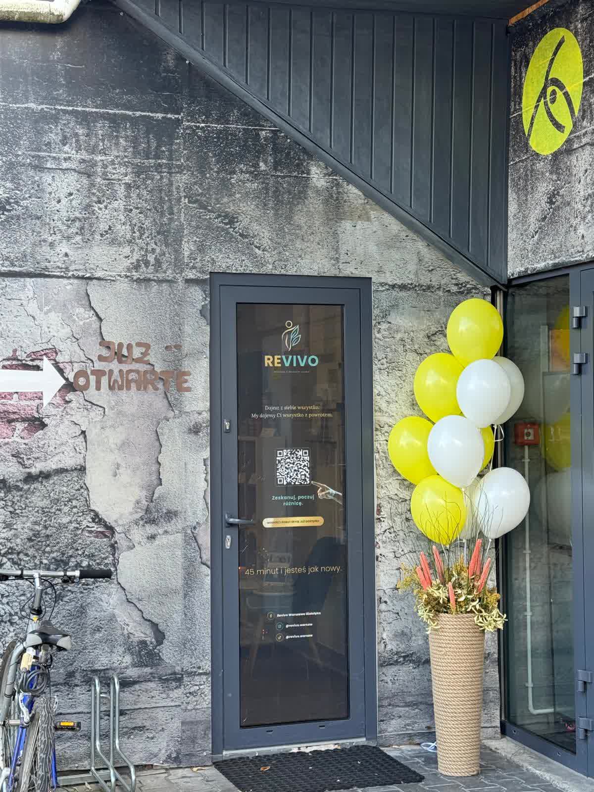 Drzwi do studia REVIVO na poziomie chodnika, obok wejścia do New Age Fitness